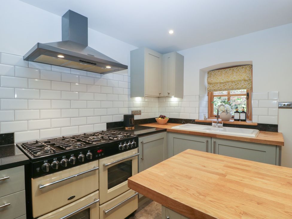 A kitchen with a stove and oven unit a wooden countertop and a sink under a window at Graig Cottage in Cwmcarn