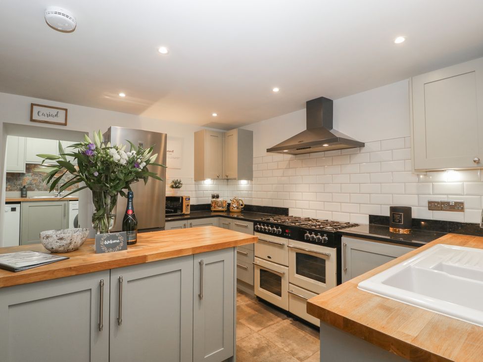 A kitchen with wooden countertops a white tiled backsplash and grey cabinets at Graig Cottage in Cwmcarn