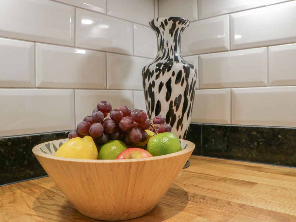 A wooden bowl with grapes lemon lime and apple on a kitchen countertop with a black and white vase against tiled backsplash at Graig Cottage in Cwmcarn