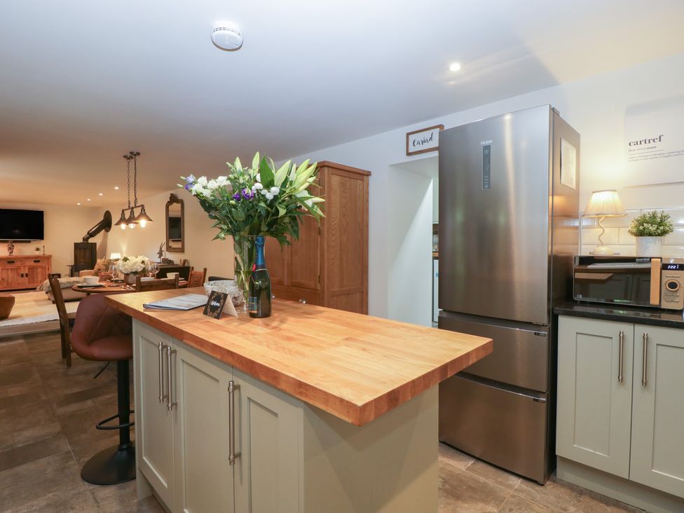 A kitchen with wooden countertop island flowers on counter stainless steel refrigerator and dining area in the background at Graig Cottage in Cwmcarn