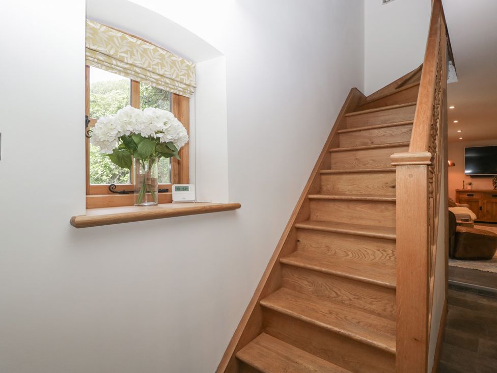 A wooden staircase next to a window with white flowers in a vase on the windowsill at Graig Cottage in Cwmcarn
