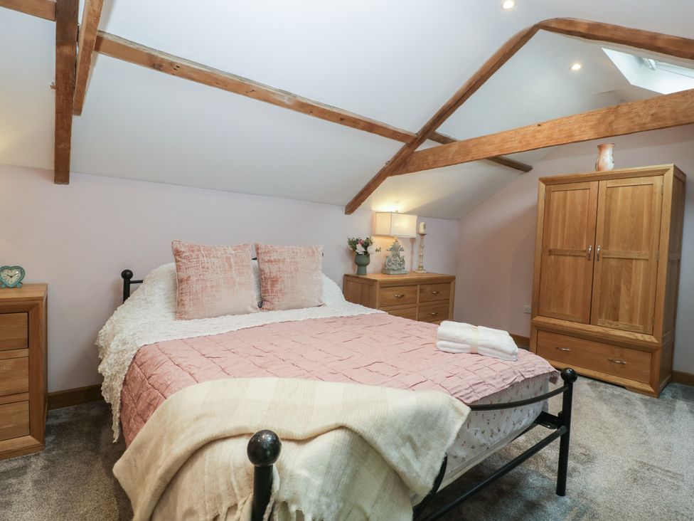 A bedroom with a double bed with pink bedding wooden wardrobe and dresser with lamp and flowers at Graig Cottage in Cwmcarn
