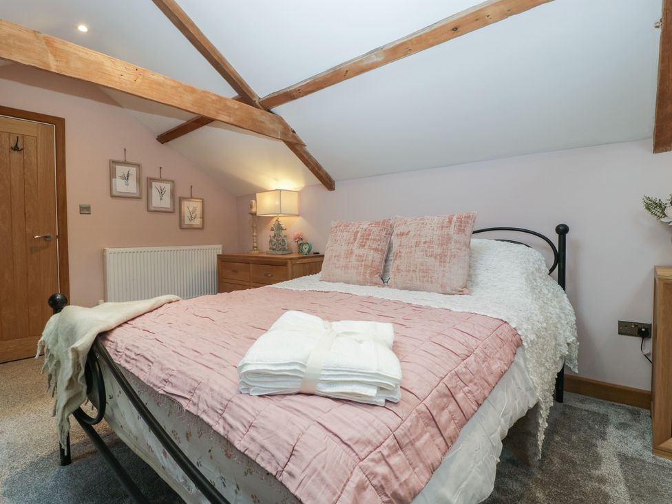 A bedroom with a bed that has pink bedding and pillows with a folded towel on top and wooden beams on the ceiling at Graig Cottage in Cwmcarn