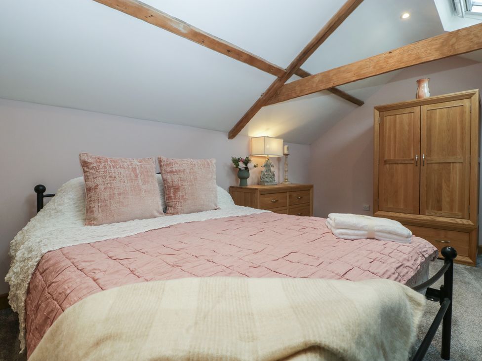 A bedroom with a bed pink pillows and quilt a wooden dresser with a lamp and flowers and a wooden wardrobe at Graig Cottage in Cwmcarn