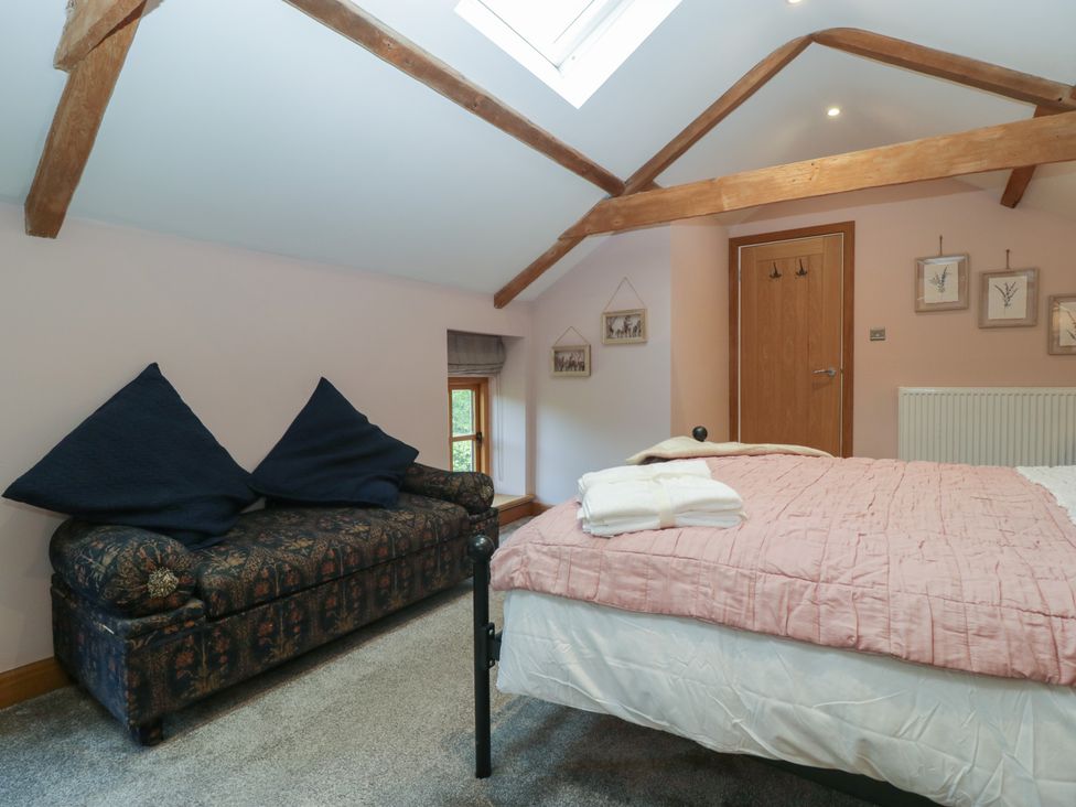 A bedroom with a bed and a sofa under wooden ceiling beams at Graig Cottage in Cwmcarn