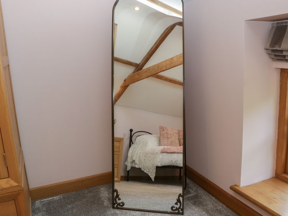 A full length mirror reflecting a bed with pillows and wooden beams on the ceiling at Graig Cottage in Cwmcarn
