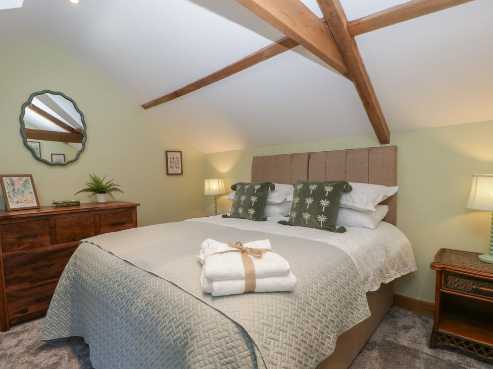 A bedroom with a double bed with green and white pillows bedside tables with lamps and a wooden dresser with a mirror at Graig Cottage in Cwmcarn