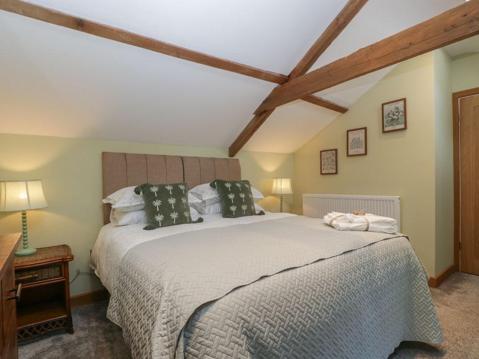 A bedroom with a bed two bedside tables with lamps exposed wooden beams and framed pictures on the wall at Graig Cottage in Cwmcarn