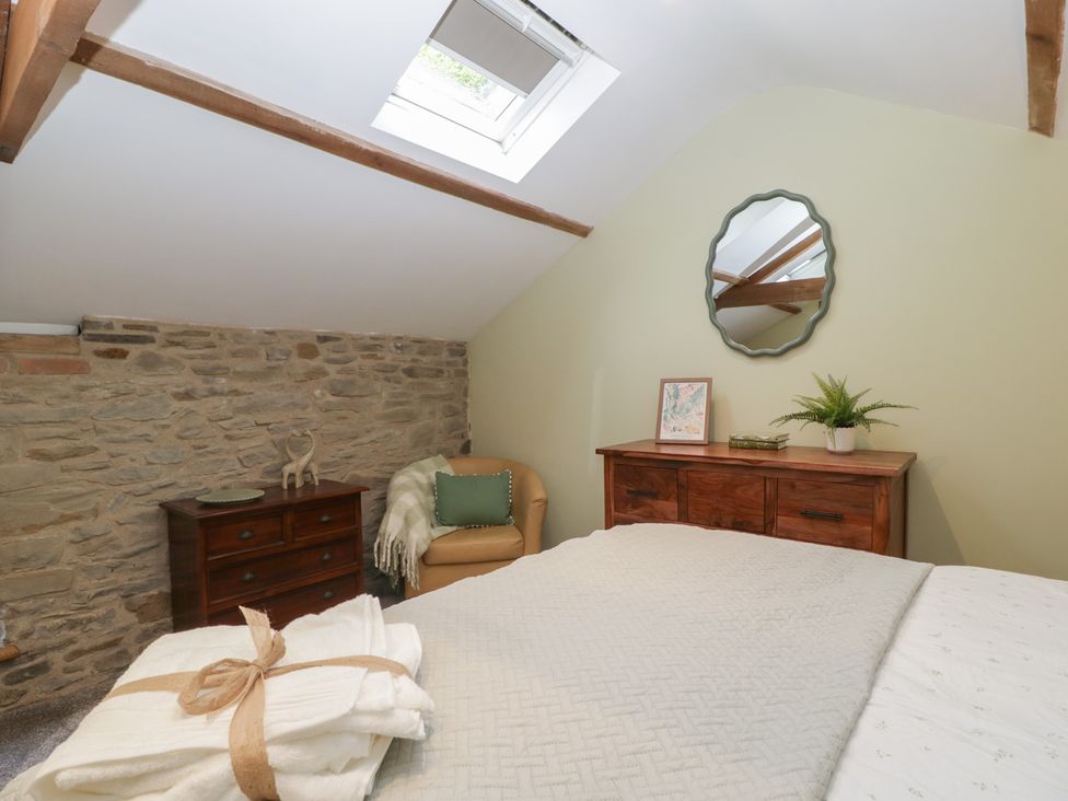 A bedroom with a bed a wooden dresser a mirror a skylight window and an armchair at Graig Cottage in Cwmcarn