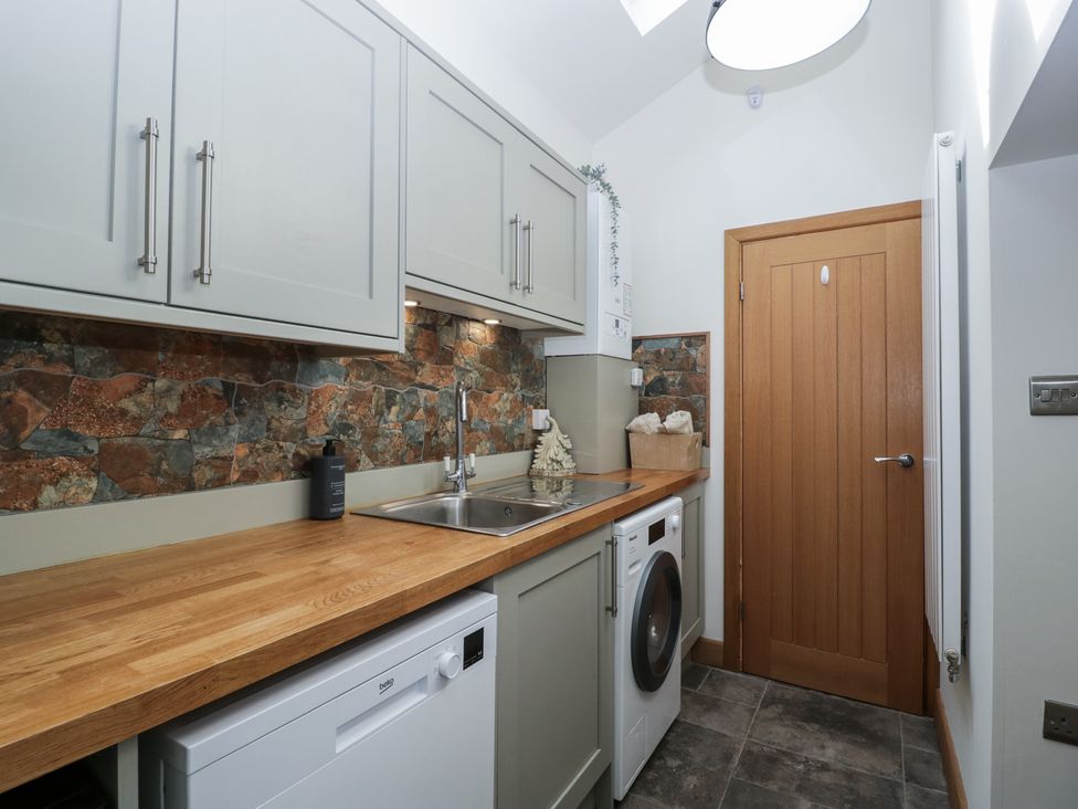 A utility room with countertop sink washing machine dishwasher and wooden door at Graig Cottage in Cwmcarn
