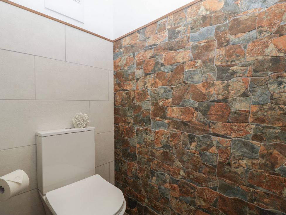 A small bathroom with a white toilet paper holder and a toilet against a stone and tiled wall at Graig Cottage Cwmcarn