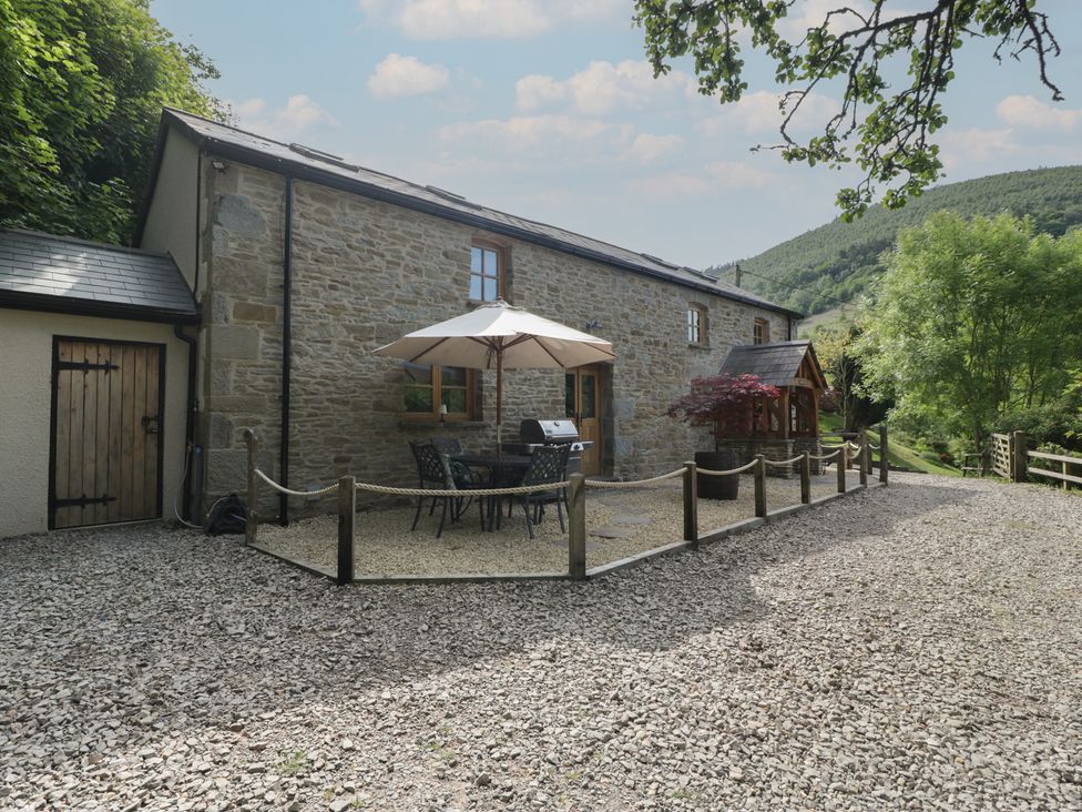 A stone house with an outdoor seating area under an umbrella and a barbecue grill at Graig Cottage in Cwmcarn