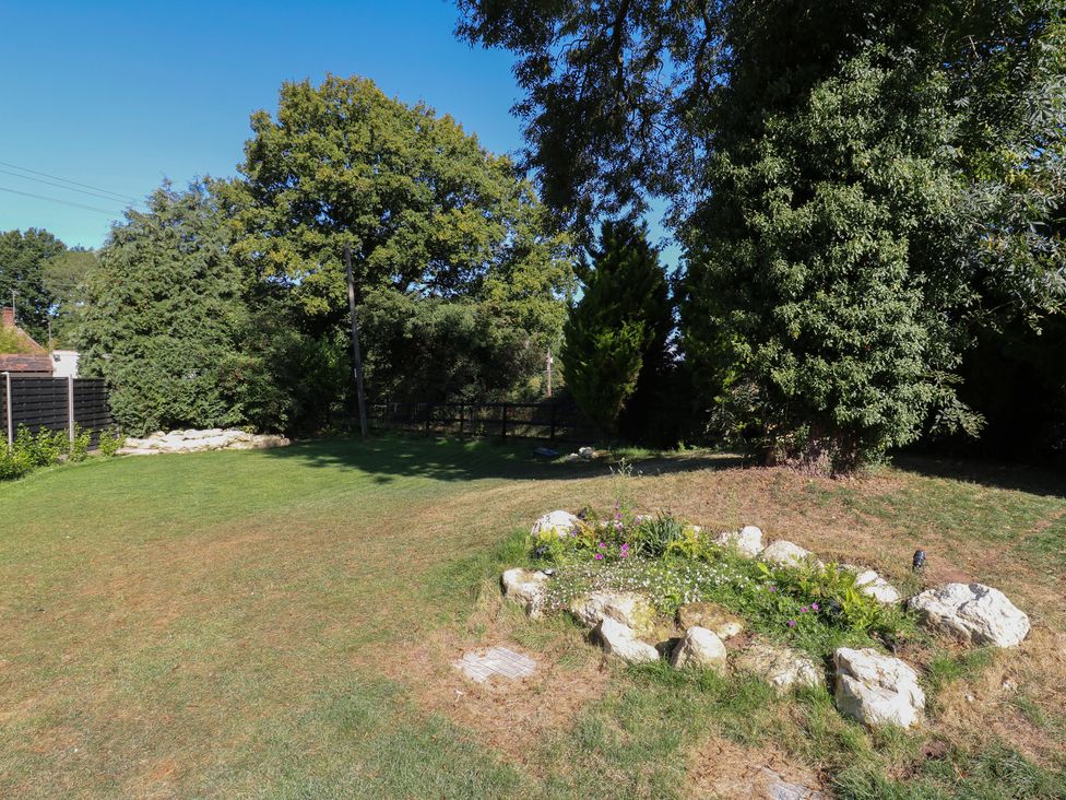 A garden with grass, trees, a flower bed, and rocks at The Old Workshop in Wormshill near Harrietsham