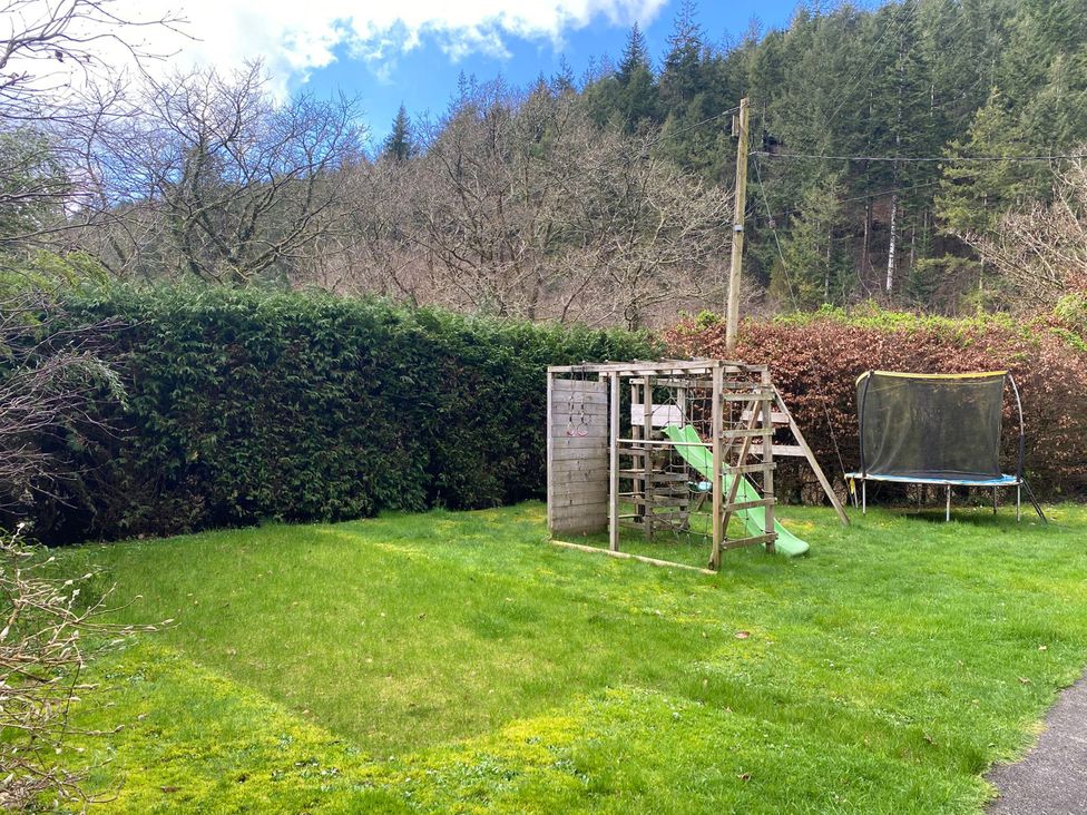 A garden with a playground structure and trampoline at Lost In The Woods Lodge near Bodmin