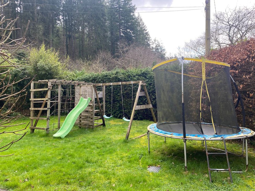A garden with a swing set, slide and trampoline at Lost In The Woods Lodge near Bodmin