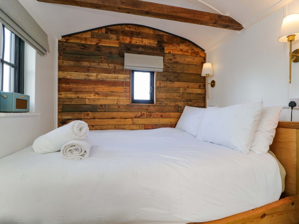 A bedroom with a bed and wooden wall at Wiltshire Weavers Hut in Sutton Benger near Christian Malford
