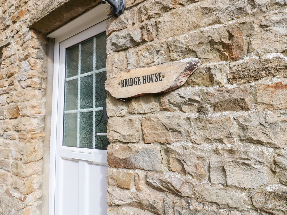 Sign for Bridge House next to a door on a stone wall