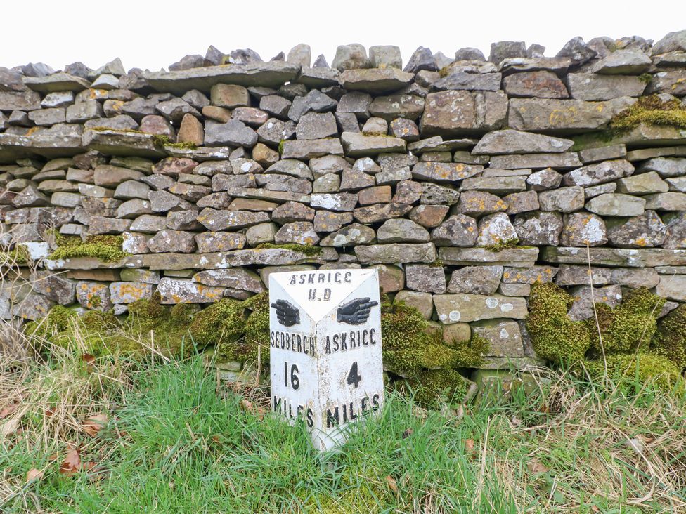 A milestone near a stone wall indicating distances to Askirice and Sedbergh at Bridge House