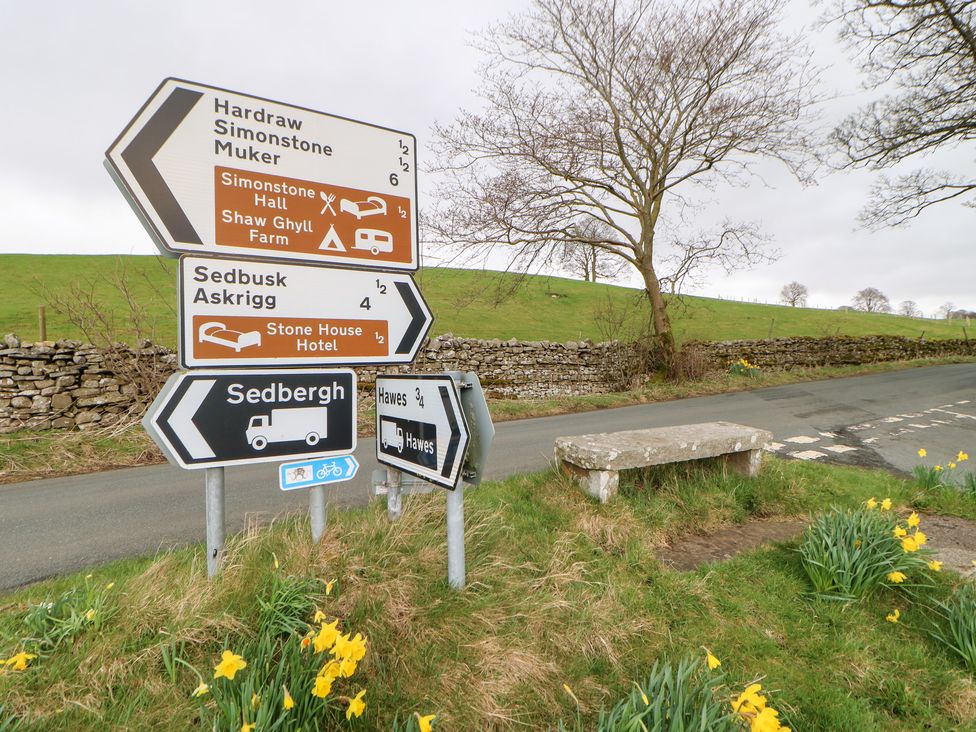Road signs indicating multiple locations near Sedbergh with daffodils in the foreground at Bridge House