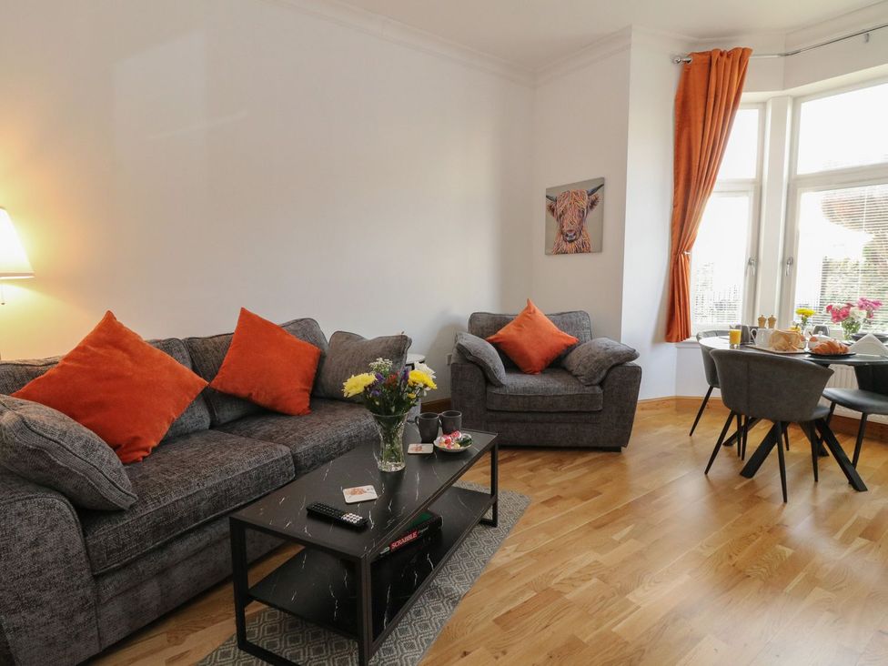 A living room with two grey sofas with orange cushions and a black coffee table at Lena's Corner in Dunoon