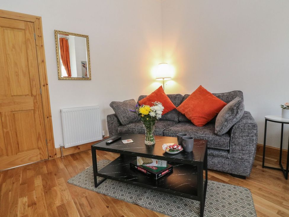 A living room with a gray sofa with orange pillows and a black coffee table with flowers at Lena's Corner in Dunoon