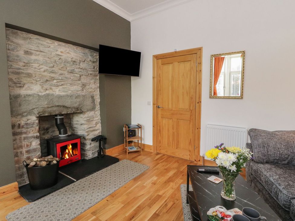 A living room with a stone fireplace and wood stove a wooden door a wall-mounted TV and a coffee table with flowers at Lena's Corner in Dunoon