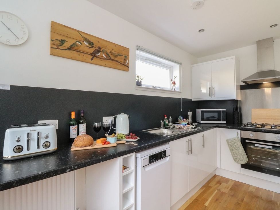 A kitchen with black countertops white cabinets a toaster wine bottles and a cutting board with bread and fruit at Lenas Corner in Dunoon