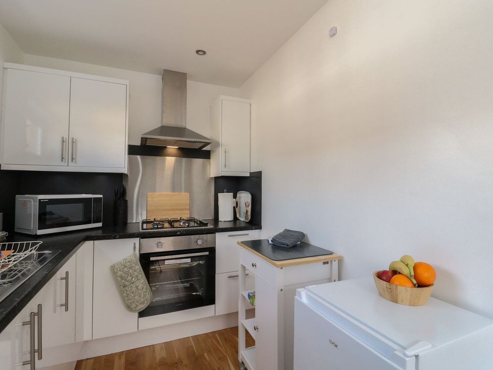 A kitchen with white cabinets a microwave an oven a stove and a small fridge with a fruit bowl at Lenas Corner in Dunoon