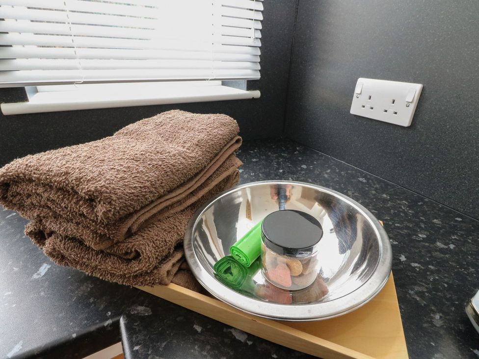 A black countertop with a folded brown towel a metal bowl containing a jar and green plastic bags and a white dual electrical socket on the wall at Lenas Corner in Dunoon