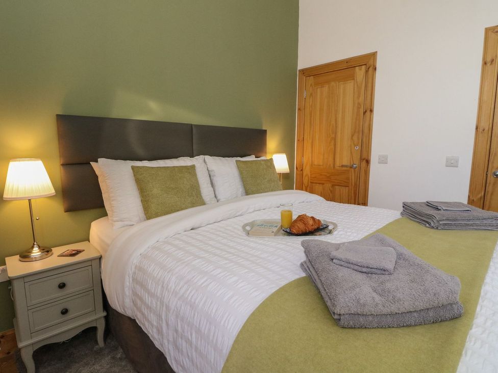 A bedroom with a double bed, two pillows, bedside table with lamp, folded towels, croissant and orange juice on tray at Lena's Corner in Dunoon