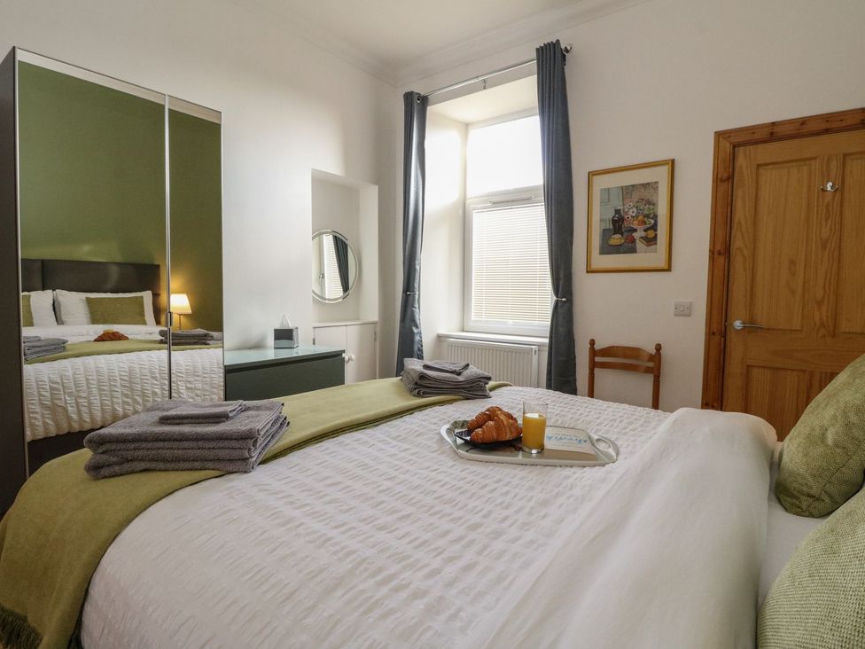 A bedroom with a made bed towels on the bed a tray with croissants orange juice and a book near window with curtains at Lena's Corner in Dunoon