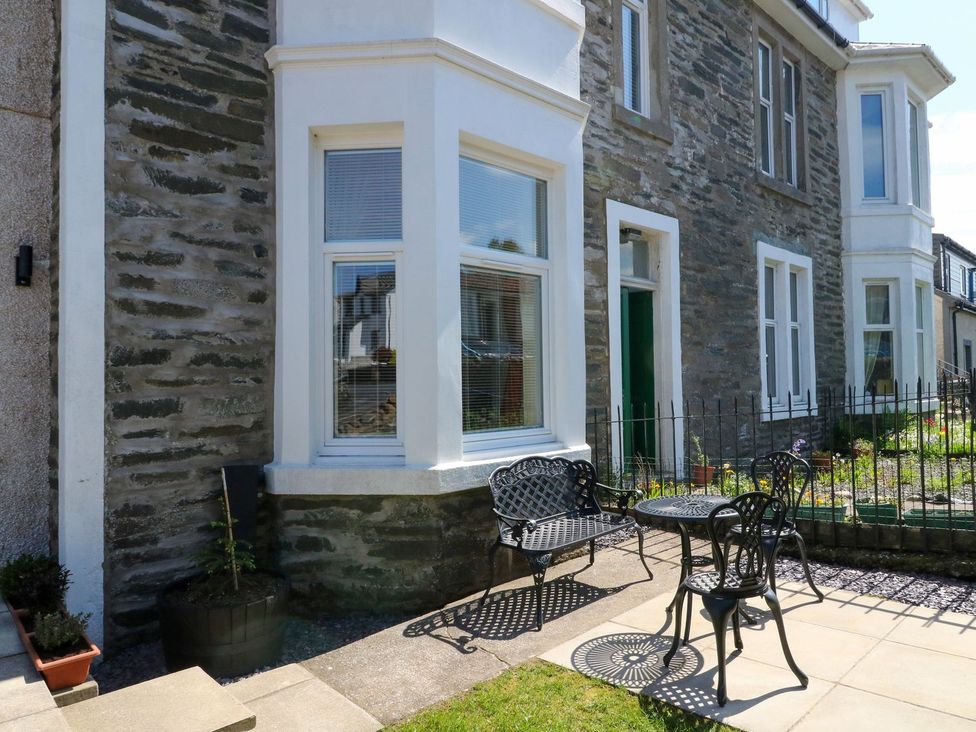 An outdoor patio area with metal table and chairs in front of a stone building with white framed windows at Lenas Corner in Dunoon
