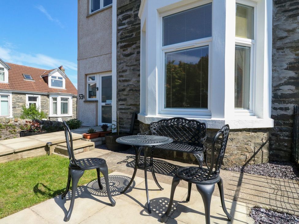 A patio with a black metal table two chairs and a bench outside a stone house at Lenas Corner in Dunoon