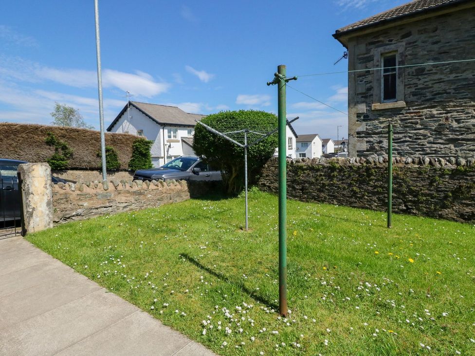 A grassy garden area with a rotary clothesline and stone wall near houses at Lenas Corner in Dunoon