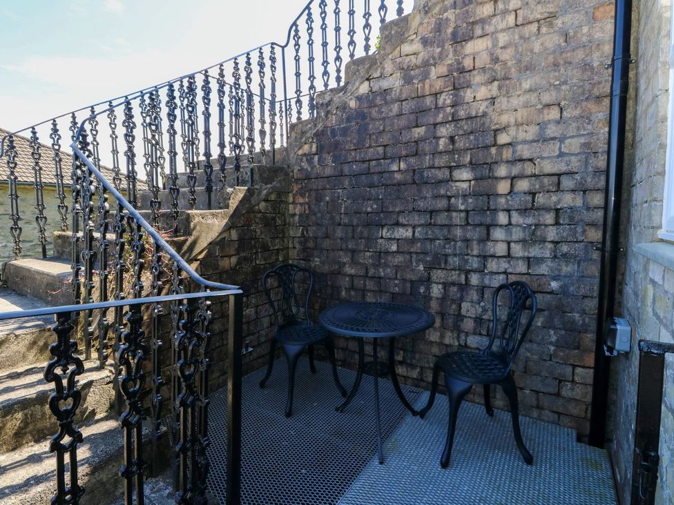 A small outdoor seating area with two black metal chairs and a round table next to a brick wall and staircase at Lenas Corner in Dunoon