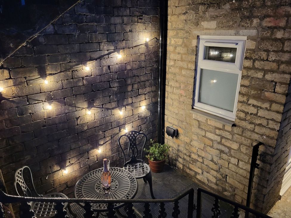 A small outdoor patio with a metal table and chairs string lights on brick walls and a potted plant at Lenas Corner in Dunoon