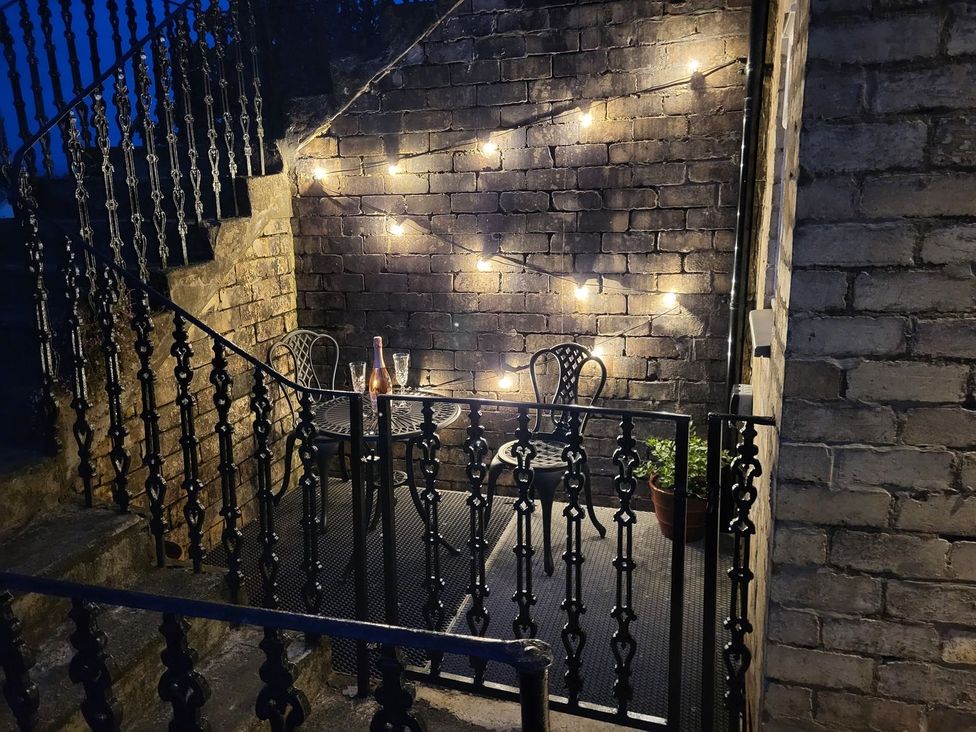 A small outdoor patio with a metal table and two chairs string lights on a brick wall and a potted plant at Lenas Corner in Dunoon