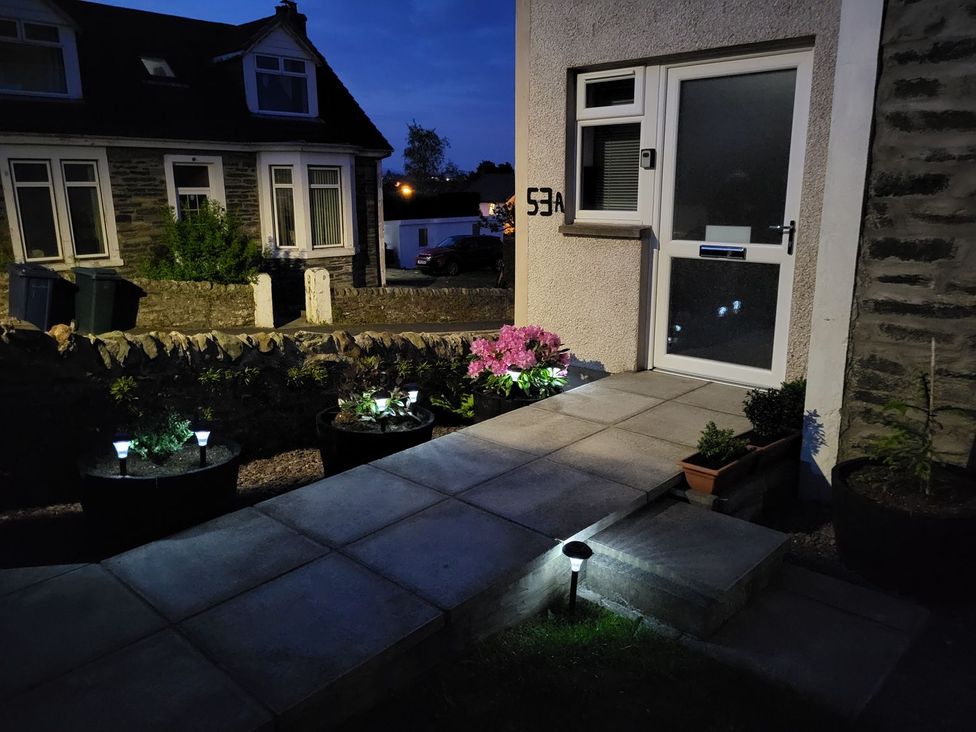An outdoor pathway with potted plants and solar garden lights leading to a white door at Lenas Corner in Dunoon