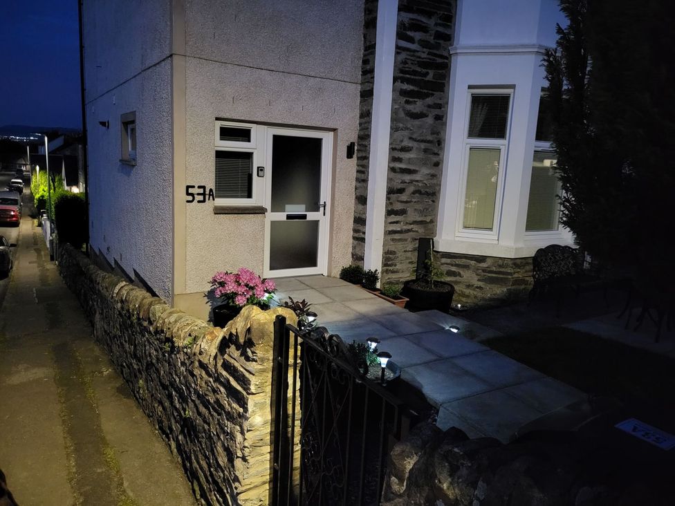 A house entrance with a white door and window at night with a stone wall and gate at Lenas Corner in Dunoon