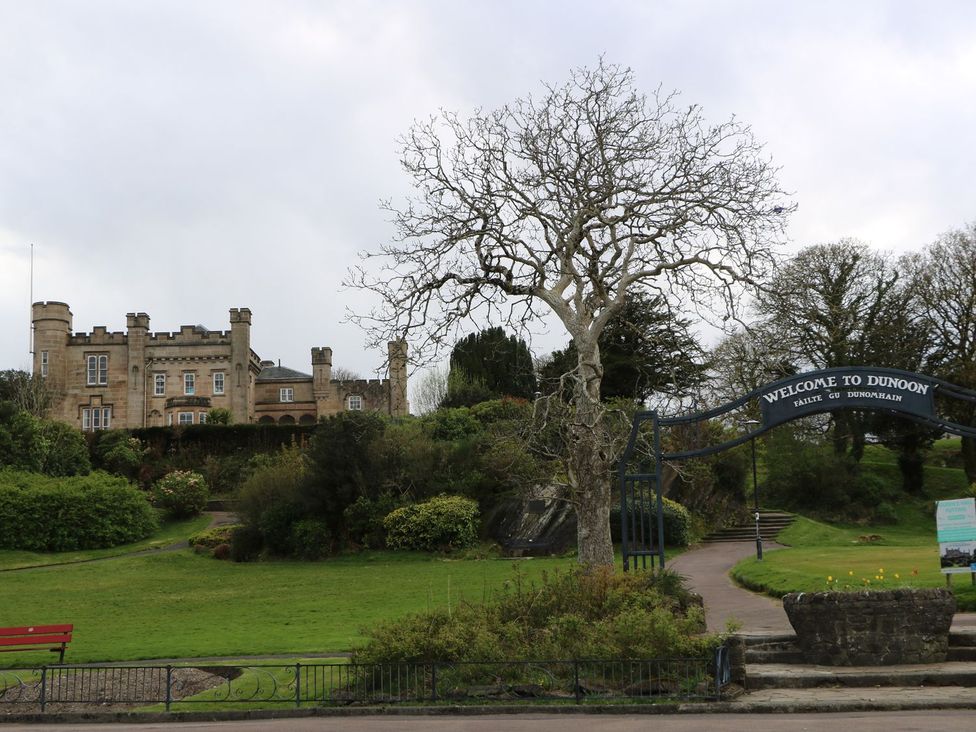 A stone building with battlements on a hill with a tree and a welcome to Dunoon sign in the foreground at Lena's Corner in Dunoon