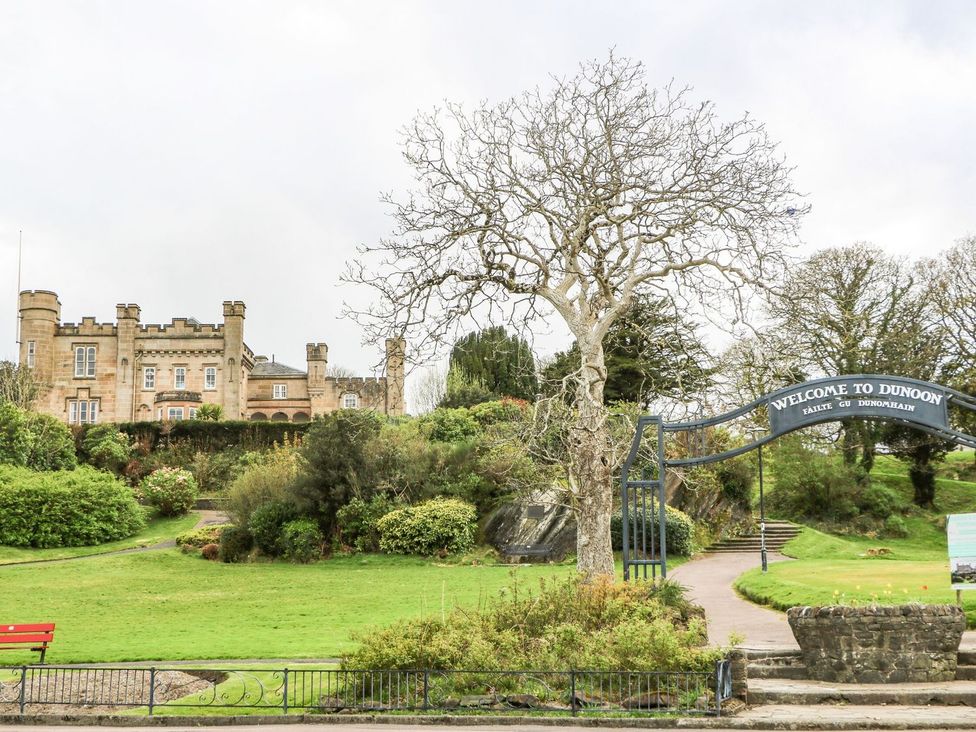 A park area with a large stone building in the background and a welcome to Dunoon sign at Lena's Corner in Dunoon