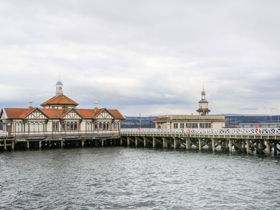 A wooden pier with two buildings over water and hills in the background at Lenas Corner in Dunoon
