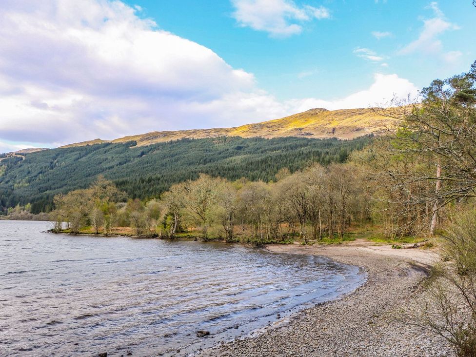 A lakeside with a pebble shore trees along the edge and hills in the background at Lenas Corner in Dunoon