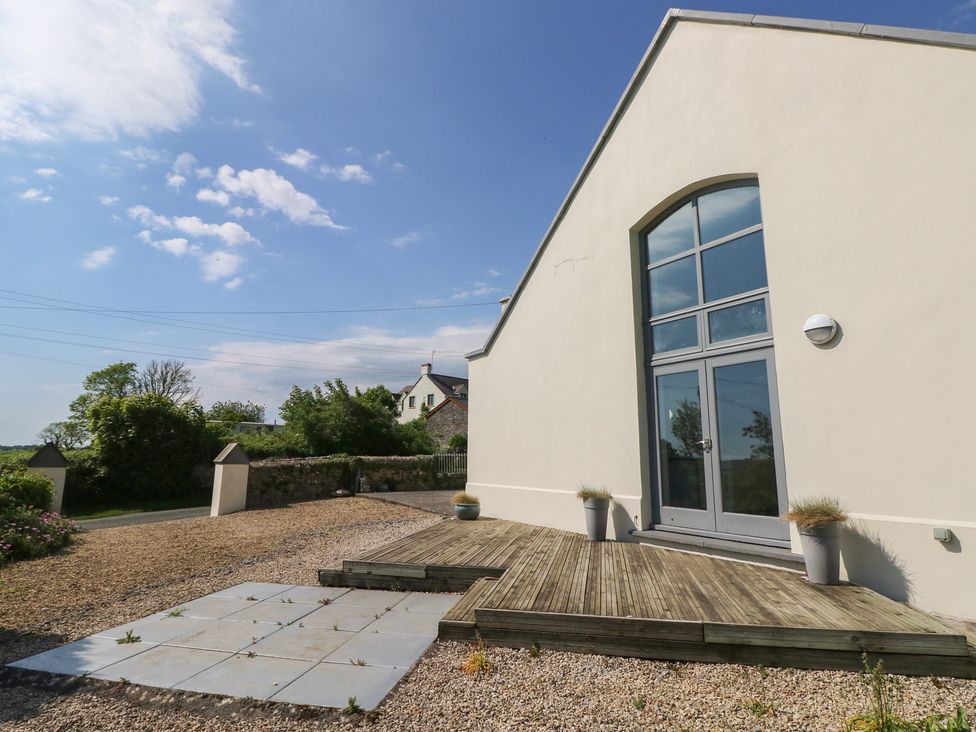 An exterior view of a building with large grey doors and windows a wooden deck with three pots on gravel at Zoar Chapel in Carew
