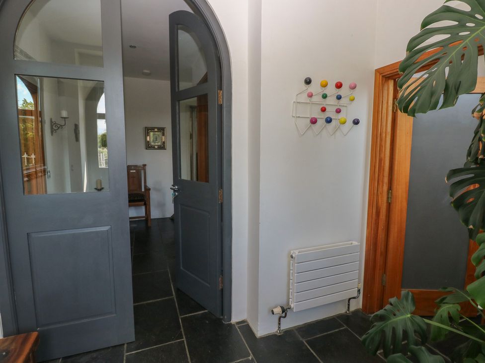An entryway with dark arched double doors a colorful coat rack on the wall a small radiator and a large leafy plant at Zoar Chapel in Carew