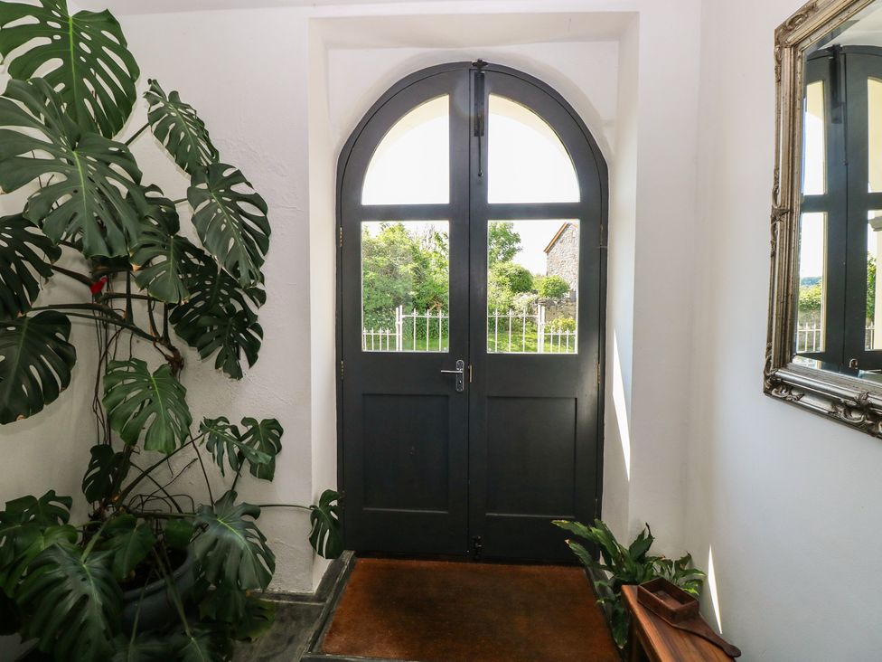 An entrance with a dark arched double door a large leafy plant a mirror on the wall and a small wooden bench at Zoar Chapel in Carew
