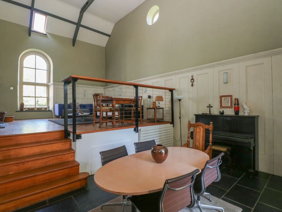 A split-level room with a dining table and chairs on the lower level and a sitting area with chairs and a table on the upper level at Zoar Chapel in Carew
