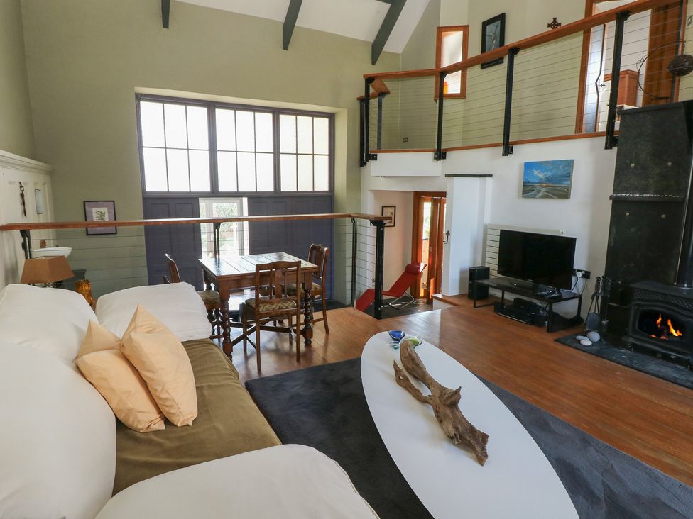 A living room with a white and green sofa a wooden dining table and chairs a television near a fireplace at Zoar Chapel in Carew