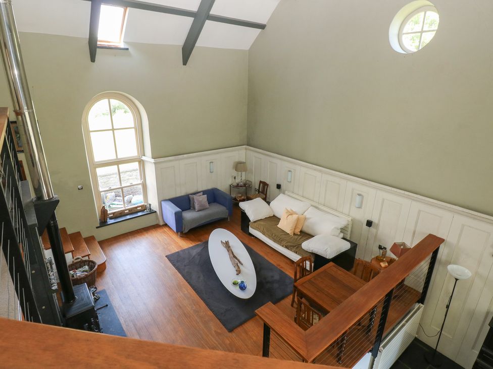 A living room with a blue armchair white sofa wooden dining table and large arched window at Zoar Chapel in Carew