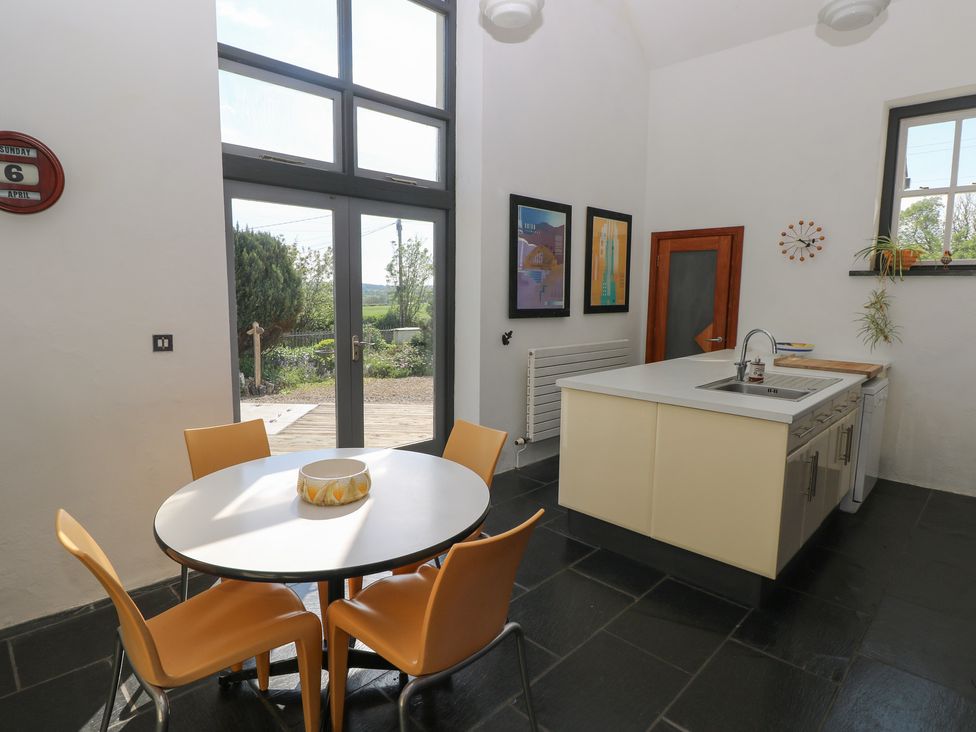 A kitchen with a round table and four chairs near glass doors and an island with a sink at Zoar Chapel in Carew